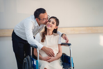 A man kisses a pregnant woman in a wheelchair.