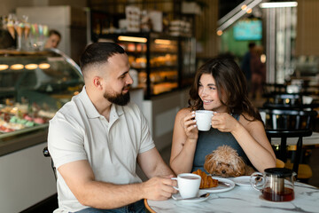 A woman with long hair with brown maltipoo and a bearded man in a cap are talking in cafe. Couple in love with little dog having meeting and waiting for breakfast in cafe.