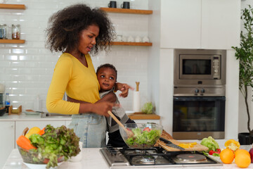 Happy African mother and son making salad while preparing food in the kitchen having fun, mother and son cooking activity concept.