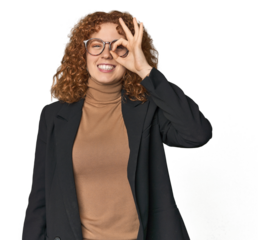 Young Caucasian redhead in business attire excited keeping ok gesture on eye.