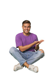 Casual man sitting on floor holding a copy space on a palm.