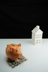 Vertical photo of a piggy bank on several yen bills next to a residential building as a concept of saving for home purchase