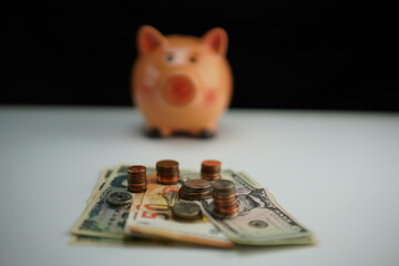 Horizontal photo of several dollar, euro and yen bills surrounded by coins of different currencies with a piggy bank out of focus in the background as a concept of saving and buying foreign currency