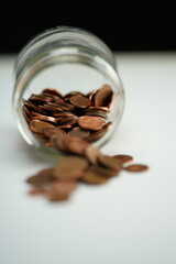 Vertical photo of coins of different currencies coming out of a jar lying on its side
