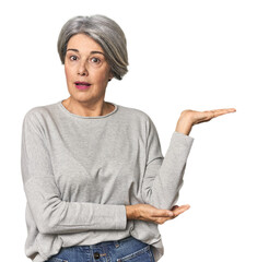 Caucasian mid-age female on studio background impressed holding copy space on palm.