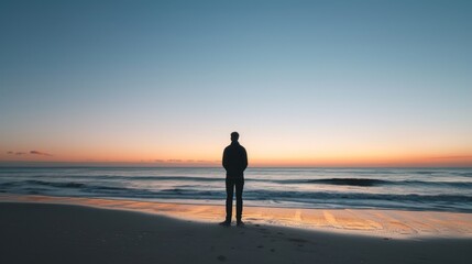 Fototapeta premium Solo traveler standing on a beach at sunset, looking out over the ocean.