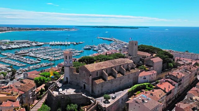 Aerial view Hilltop Gothic-style stone church with city views in Cannes. Aerial view of Cannes Port on the French Riviera, Cote d'Azur with ships and boats.