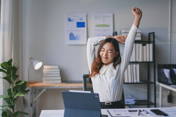 Young asian businesswoman is taking a break from work, stretching her arms and back at her desk