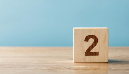 Wooden cube with number 2 two on wooden table with blue wall on background. Close-up.