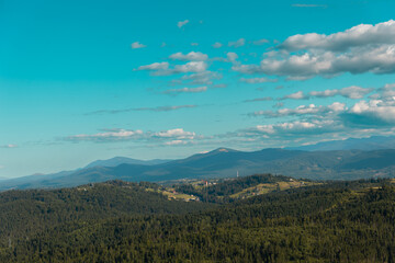 Panoramic view of a lush green mountain range under a blue sky. A breathtaking panoramic view of a lush green mountain range stretching under a bright blue sky dotted with white fluffy clouds.