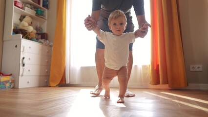 Daddy and baby taking the first steps. Child-father concept. A baby is taking the first steps on its legs. Dad teaches baby to help the little one take his first life steps in.