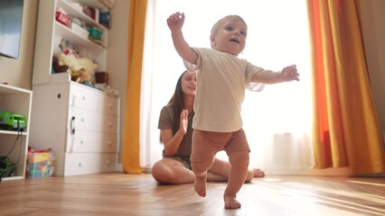 The first steps baby of learning to walk in home. Child toddler family concept. A baby is taking...