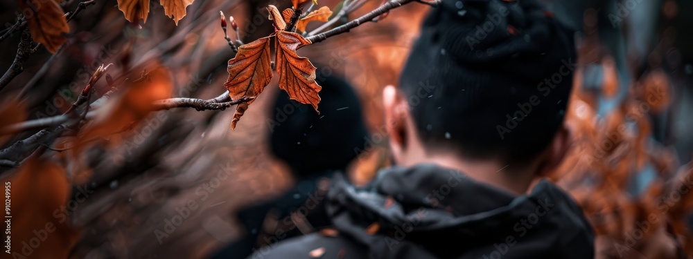 Canvas Prints  A woman poses before an orange-leafed tree, its branches framing her In the backdrop, a man is visible