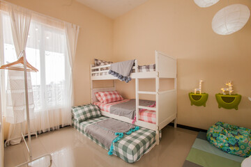 Interior of children room with white bunk bed. Modern house bedroom decoration with three kid beds, plaid bed sheets, pompom blankets, animal night lamps, sunlight through the window.