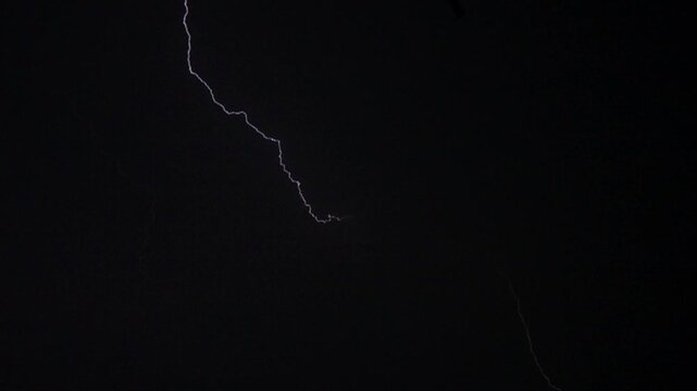Flashes of lightning in the night sky among thunderclouds.
