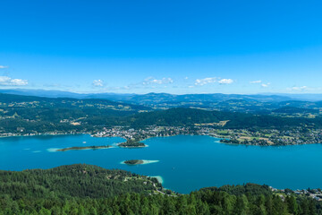 Fototapeta premium Aerial panoramic view of Lake Wörthersee seen from Pyramindenkogel in Carinthia, Austria. Serene turquoise waters, lush green forests and rolling hills of Austrian Alps. Charming lakeside village