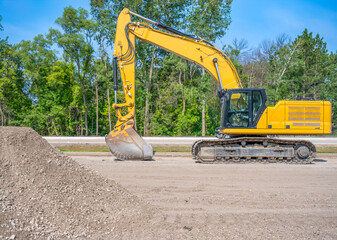 Aggregate dirt pile at a construction site with a defocused excavator bucket in the background.