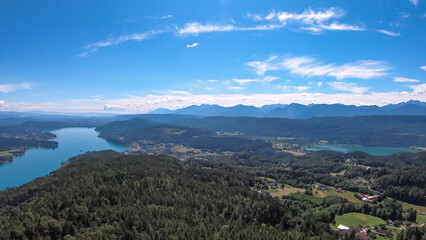 Fototapeta premium Aerial panoramic view of Lake Wörthersee seen from Pyramindenkogel in Carinthia, Austria. Serene turquoise waters, lush green forests and rolling hills of Austrian Alps. Charming lakeside village