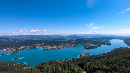 Fototapeta premium Aerial panoramic view of Lake Wörthersee seen from Pyramindenkogel in Carinthia, Austria. Serene turquoise waters, lush green forests and rolling hills of Austrian Alps. Charming lakeside village