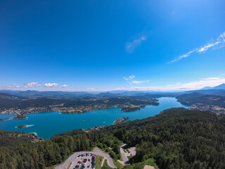 Obraz premium Aerial panoramic view of Lake Wörthersee seen from Pyramindenkogel in Carinthia, Austria. Serene turquoise waters, lush green forests and rolling hills of Austrian Alps. Charming lakeside village