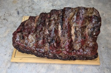 Cooked long ribs in one piece on wooden plate, stone background