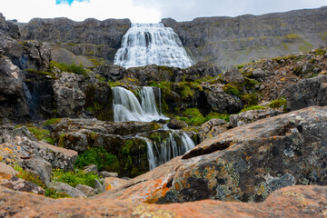 Obraz premium Cascades of Dynjandi Foss, a beautiful huge waterfall in the westfjords of Iceland with red rock in the foreground