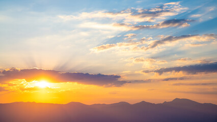 The setting sun over the mountains, the beautiful sun's rays shine through the clouds, the natural background, freedom, tranquility and peace