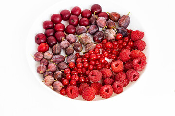 A mixture of red summer berries on white plate, top view. Tasty fresh ripe red currant, raspberry, gooseberry, cherry berries. Healthy food texture on white background.