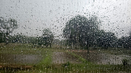 Raindrops on a window with a blurred view of flooded fields and trees, capturing the essence of a heavy rainstorm
