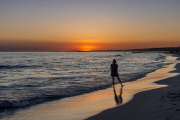 Sunset on Son Bou beach with the silhouette of a girl, a golden horizon with the sun setting over the sea. Menorca, Spain