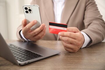Man with credit card and smartphone at wooden table, closeup