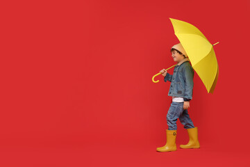 Little boy with yellow umbrella on red background, space for text