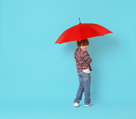 Little boy with red umbrella on light blue background, space for text