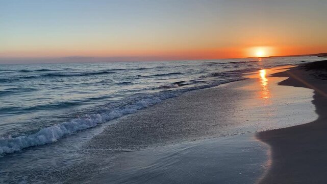 Sunset on Son Bou beach, a golden horizon with the sun setting over the sea. The long golden sandy beach reflects the warm tones of the sunset, while the gentle waves break on the shore. Menorca,Spain