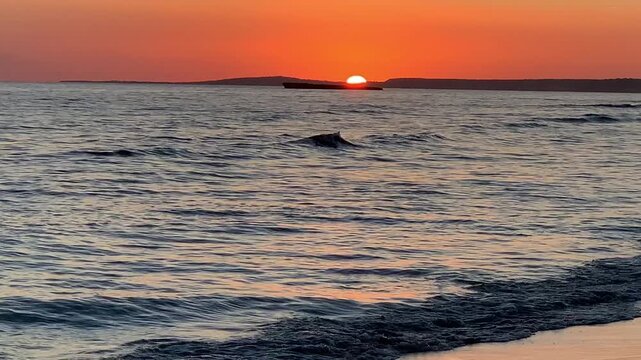 Sunset on Son Bou beach, a golden horizon with the sun setting over the sea. The long golden sandy beach reflects the warm tones of the sunset, while the gentle waves break on the shore. Menorca,Spain