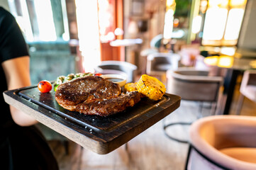Close-up of a juicy steak with grilled vegetables on a wooden serving board held by a waiter in a restaurant setting. Perfect for food, dining, and culinary themes