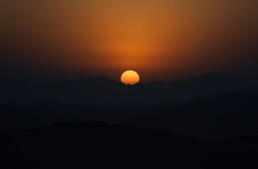 Obraz premium beautiful sunset over the hills, with a dark sky and orange sun in view