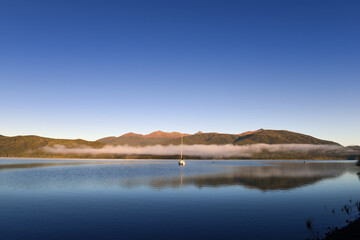 Tranquil morning at the Lake Te Anau with reflections in the water and clouds in the mountains, Fiordland, South Island, New Zealand
