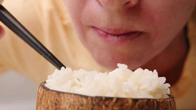 Man eats boiled rice from bowl with chopsticks close-up.