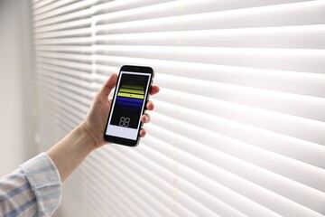 Woman using smartphone to adjust window blinds indoors, closeup. Space for text