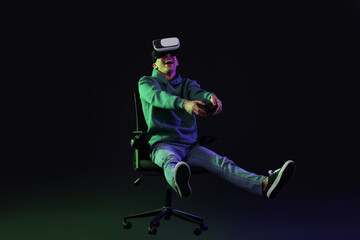 Happy young man with virtual reality headset and controller sitting on chair in neon lights against black background