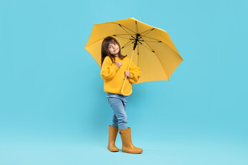 Cute little girl with yellow umbrella on light blue background