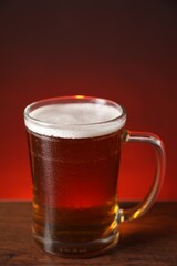 Mug with fresh beer on wooden table against color background