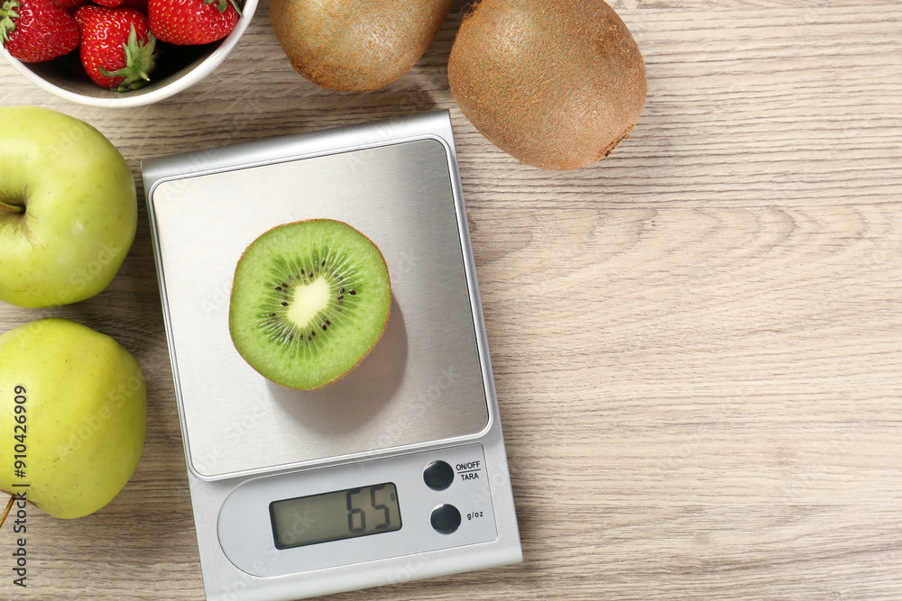 Poster Kitchen scale with piece of kiwi, apples and strawberries on light wooden table, flat lay. Space for text