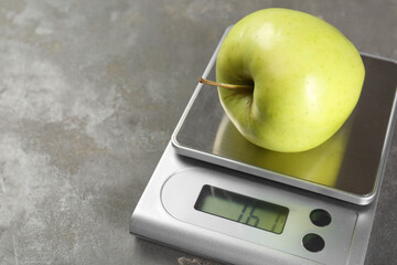 Kitchen scale with apple on grey textured table, closeup. Space for text