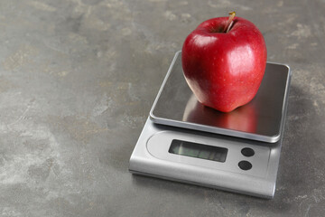 Kitchen scale with apple on grey textured table, closeup. Space for text