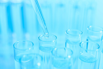 Dripping liquid from pipette into test tube on light blue background, closeup