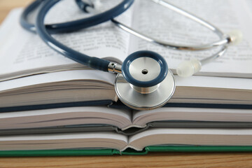 One new medical stethoscope and books on wooden table, closeup