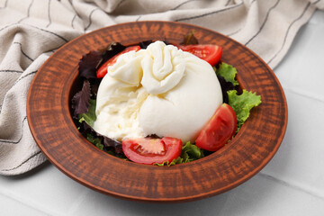 Delicious burrata salad in bowl on white tiled table, closeup