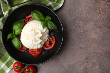 Delicious burrata cheese, tomatoes and basil in bowl on brown table, top view. Space for text